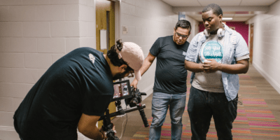 Film crew showing a young Black man how to use equipment