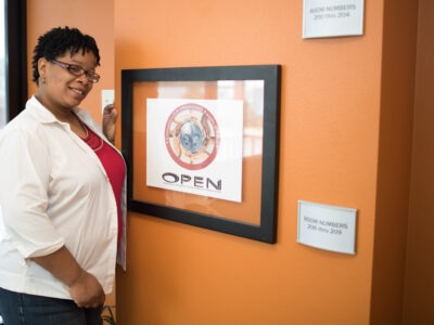 Mischell Davis stands in front of a framed sign for the Orleans Public Education Network