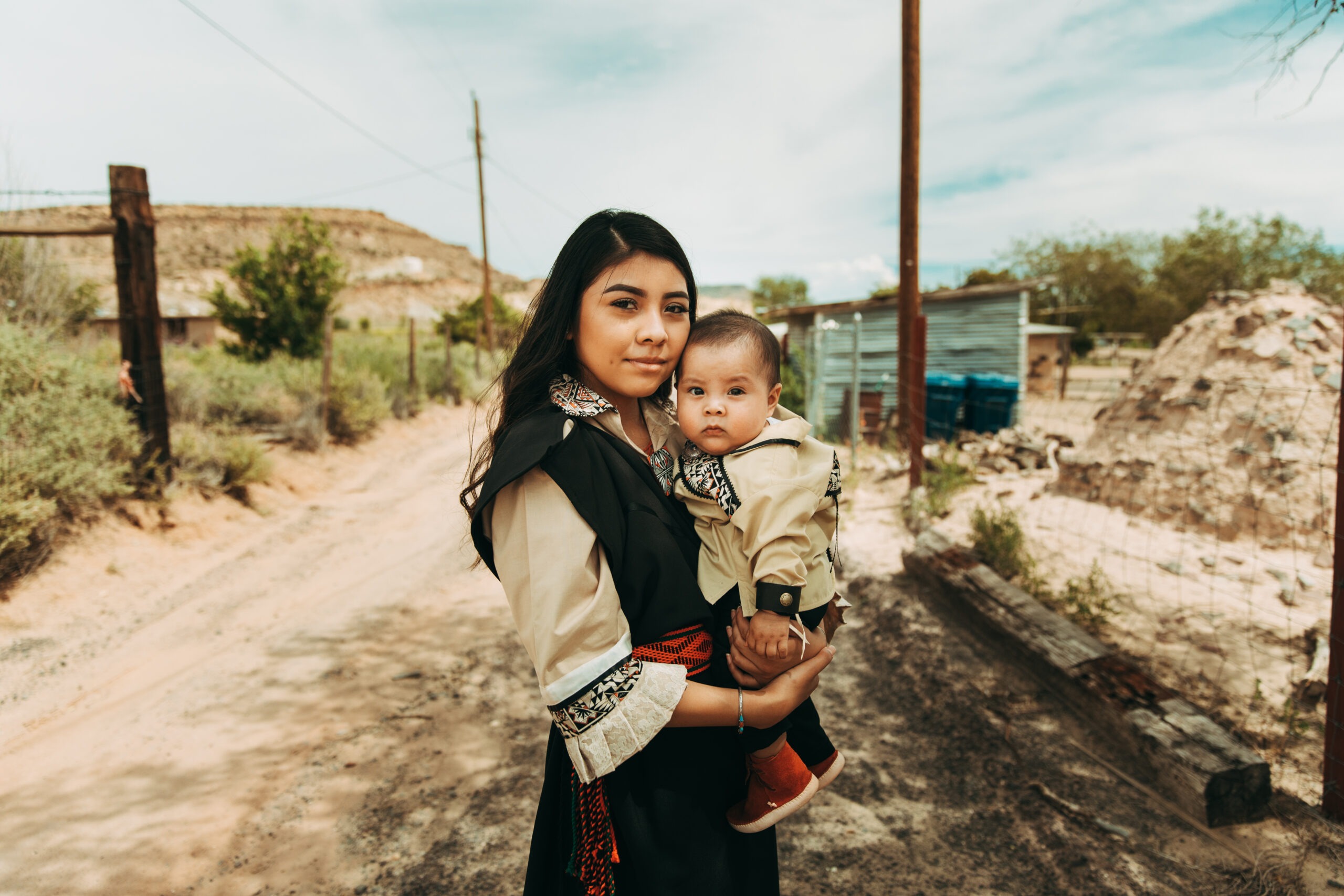 Mother holding her infant while wearing one of IWR's dresses.