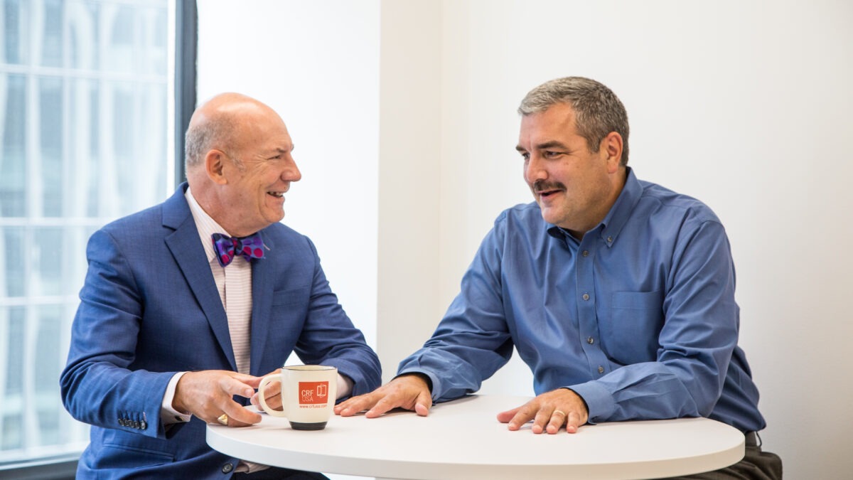 Frank Altman and Keith Rachey sit at a table for a meeting.