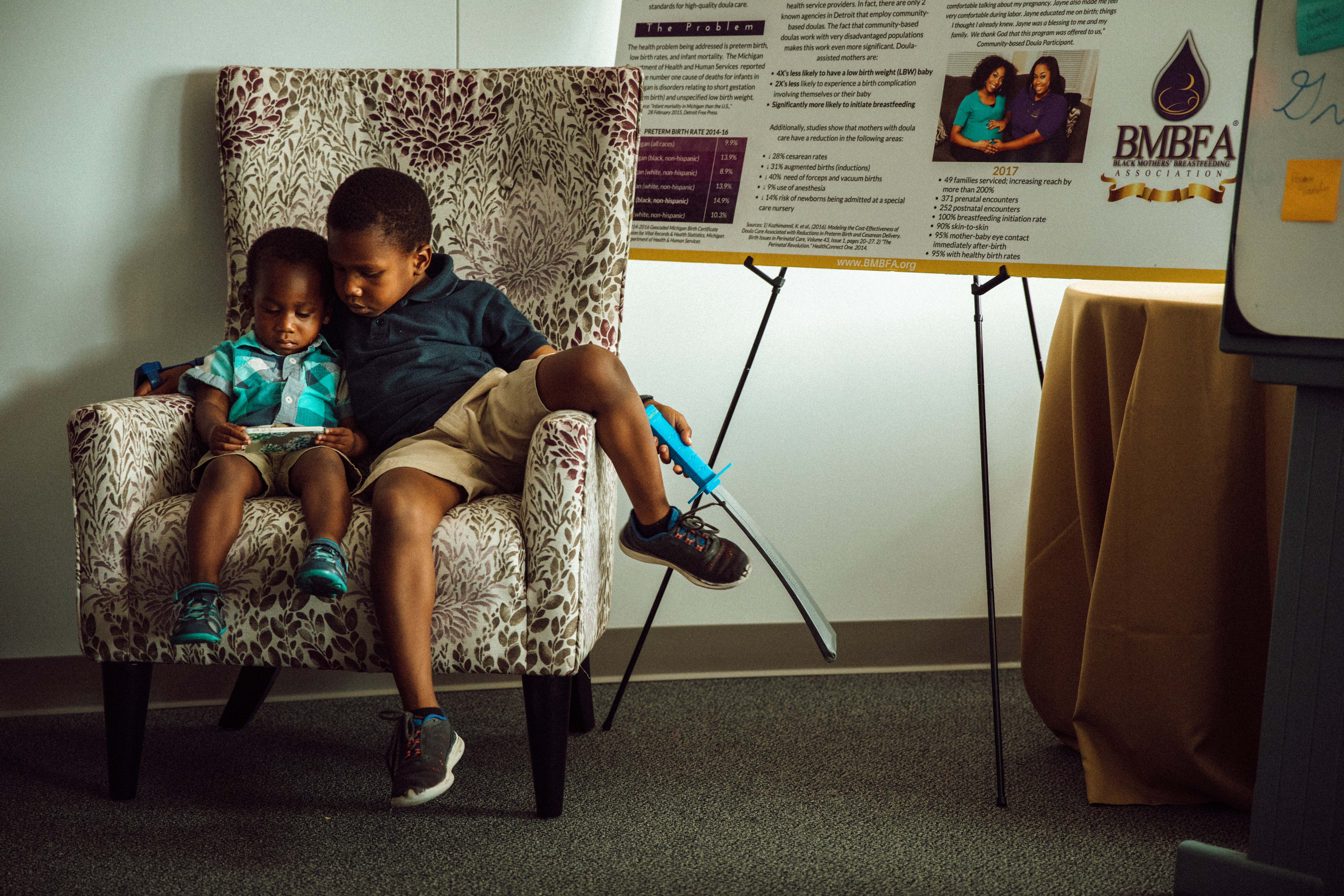Malikah Garner's two sons sitting on a chair in an office and playing on a electronic device.