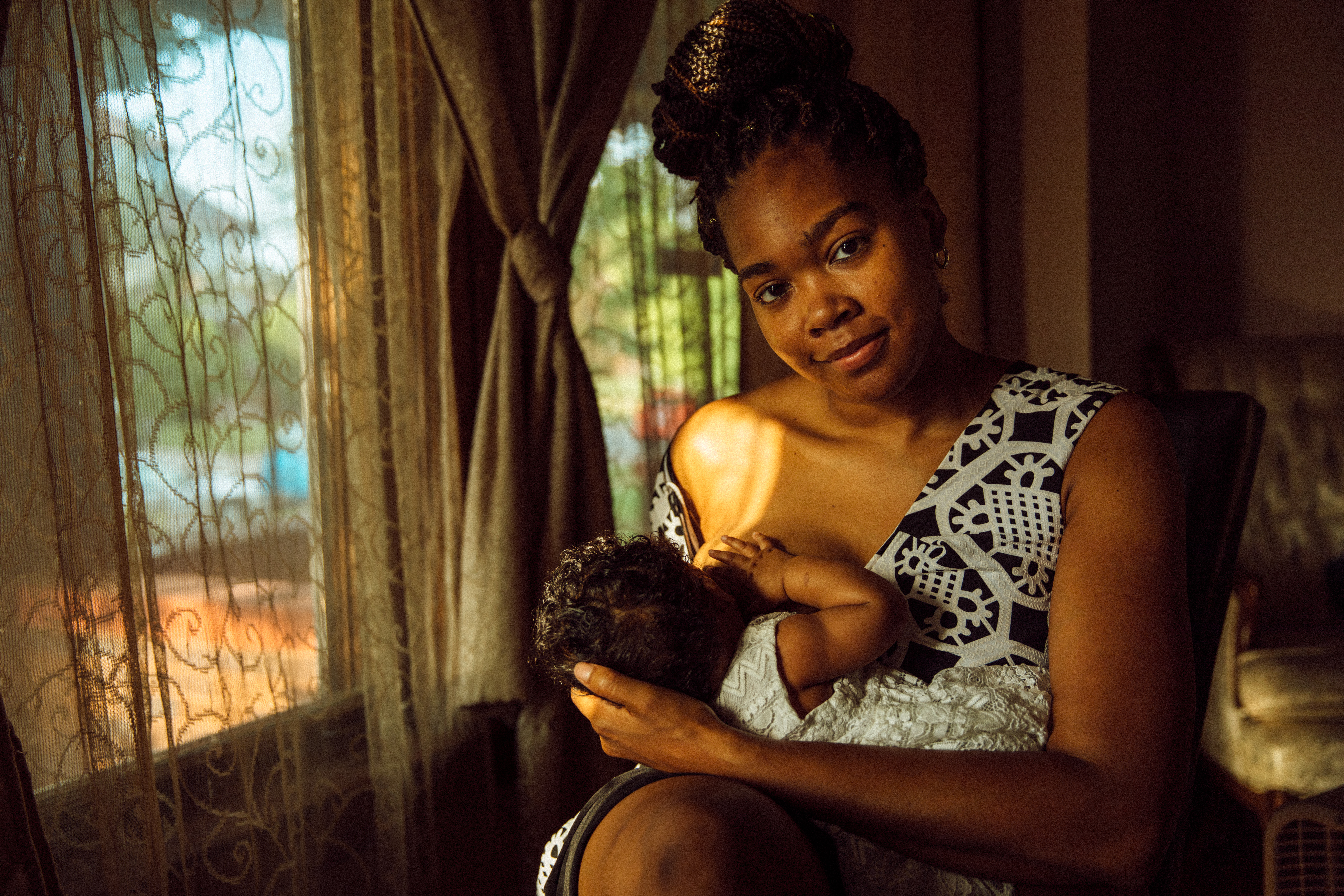 Shardaya Fuquay sits by the window to breastfeed her baby inside her Detroit home.
