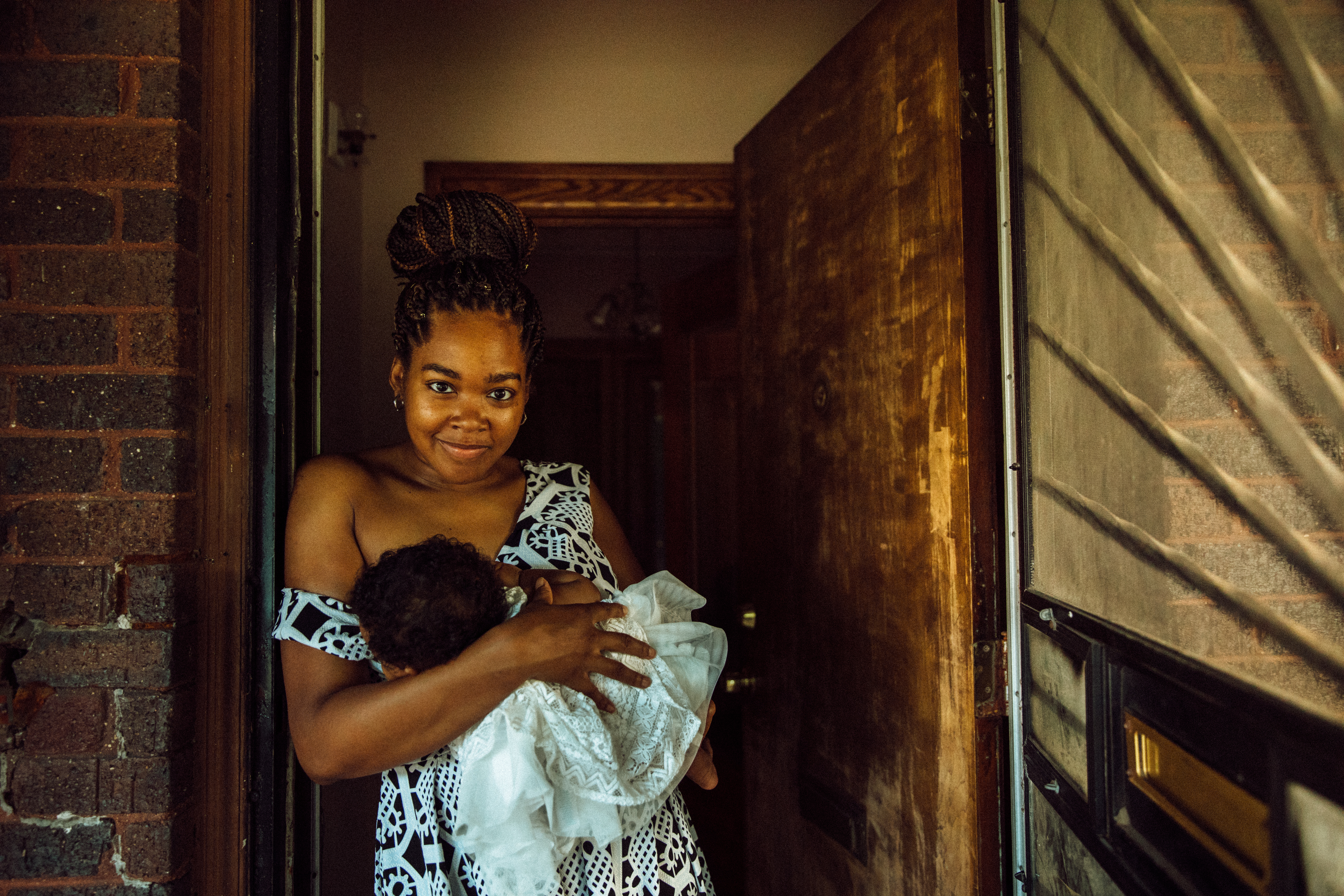 Shardaya Fuquay stands in the doorway of her house, breastfeeding her daughter.