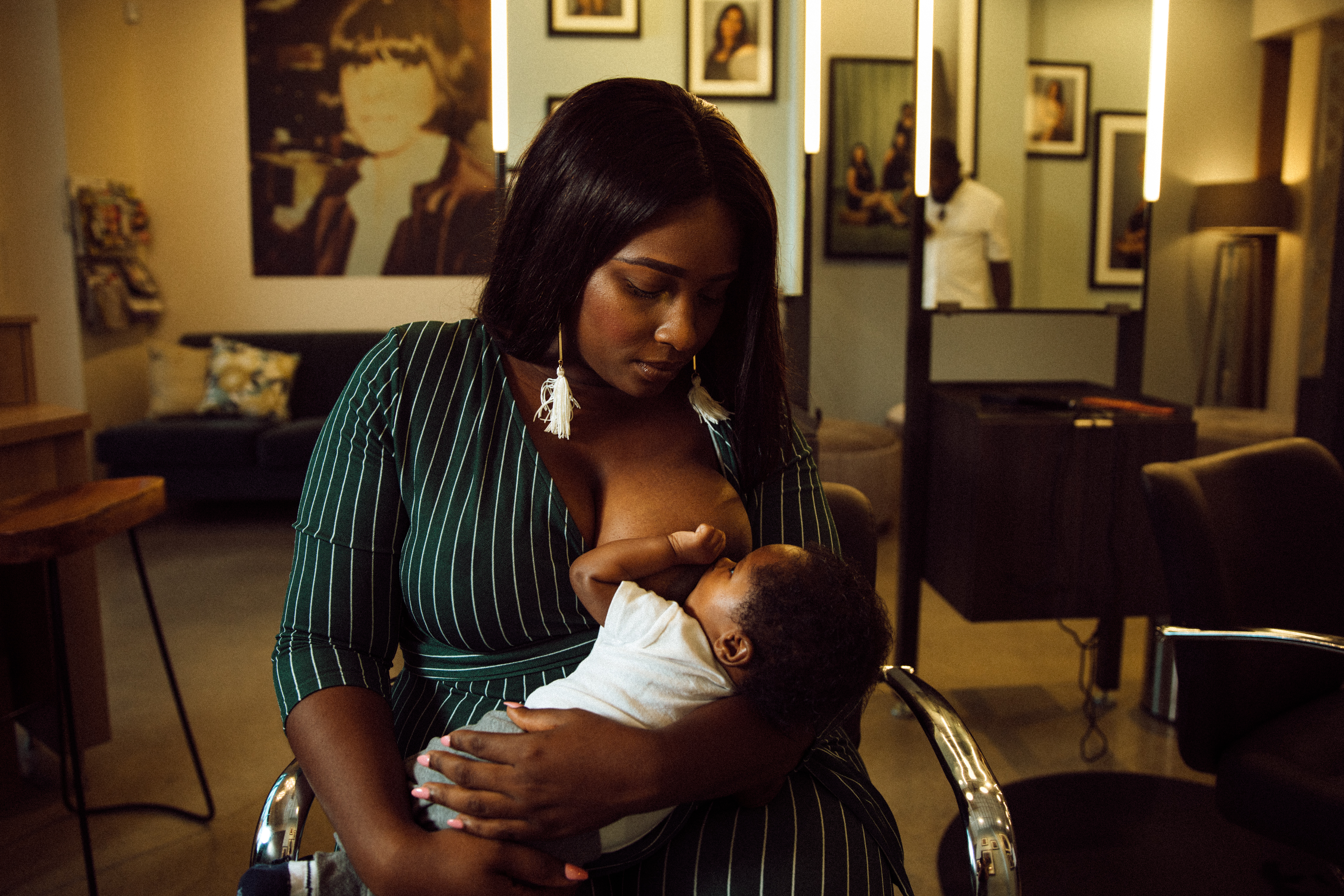 Diamond Massey breastfeeds her infant child while sitting in a hair salon chair.