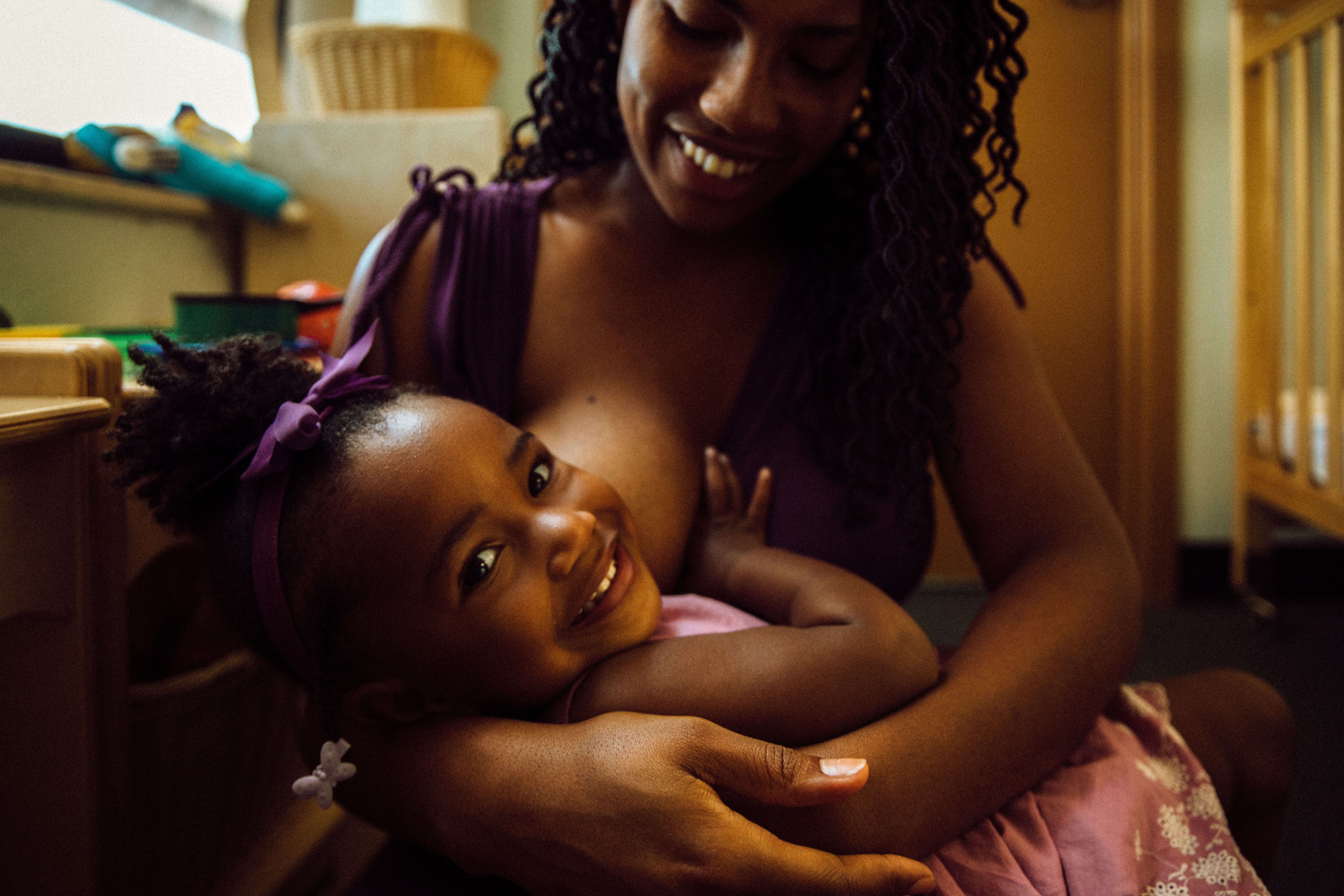 Victoria Washington holds her daughter on her lap to breastfeed. Her daughter looks back and smiles at the camera.
