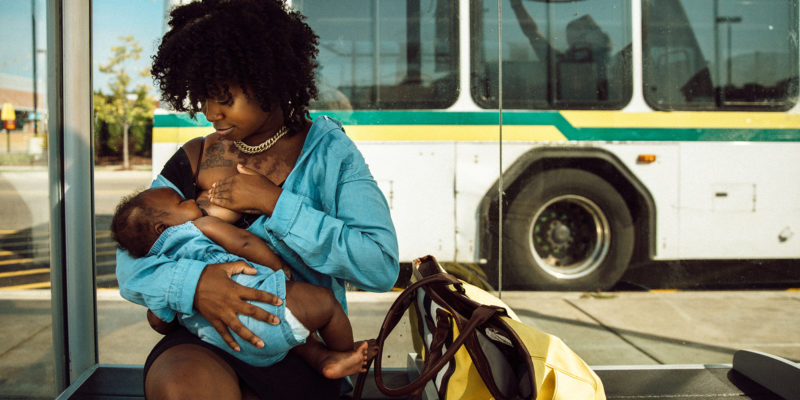 Janel Vee breastfeeds her infant daughter outside at a bus stop.