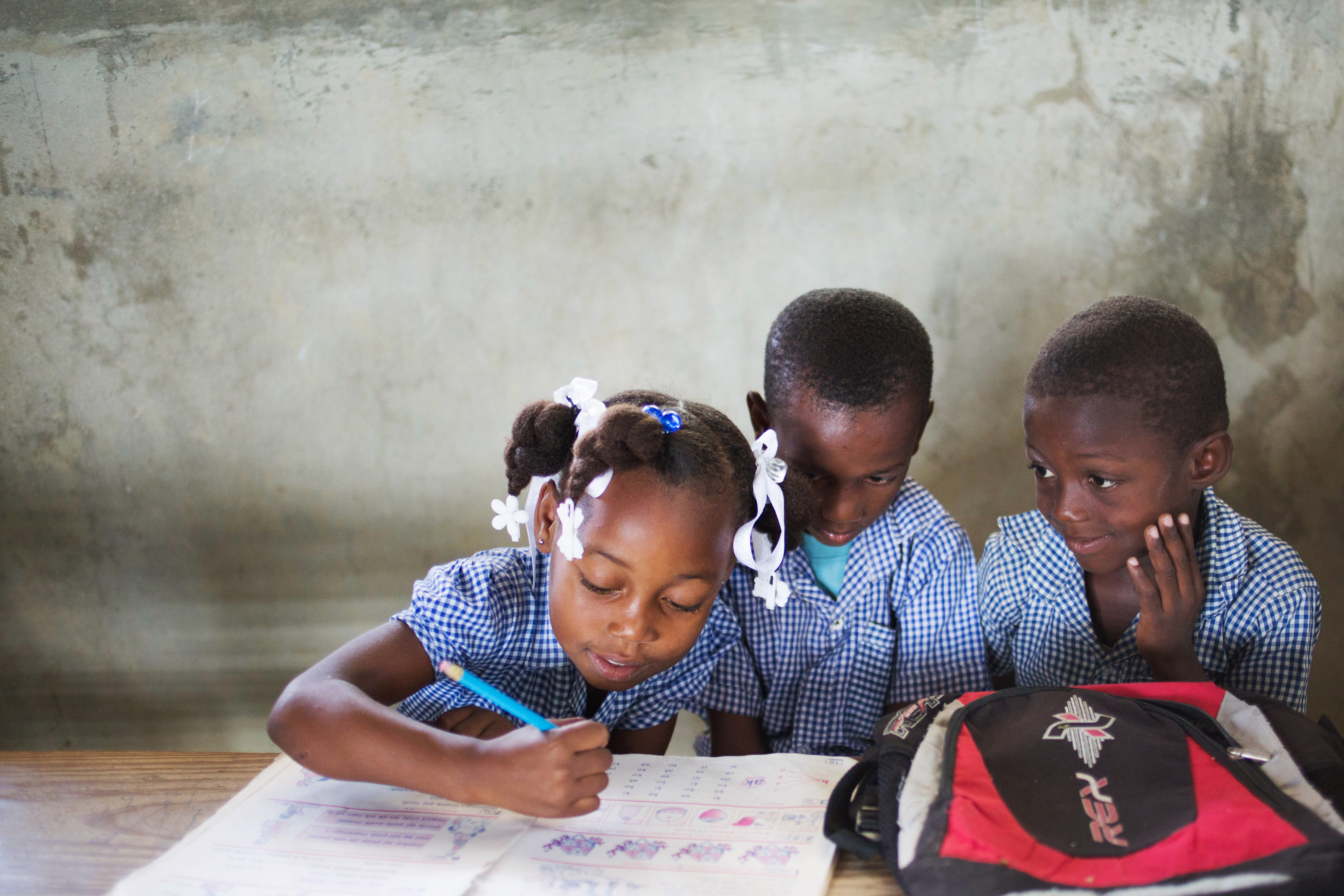 Educational Access - Three students in Haiti working on their assignment in a classroom.