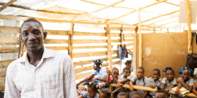 A teacher in Haiti poses with his classroom in the background.