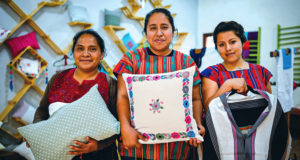 Three Indigenous women in Chiapas, Mexico, holding textile goods such as pillows and shirts.