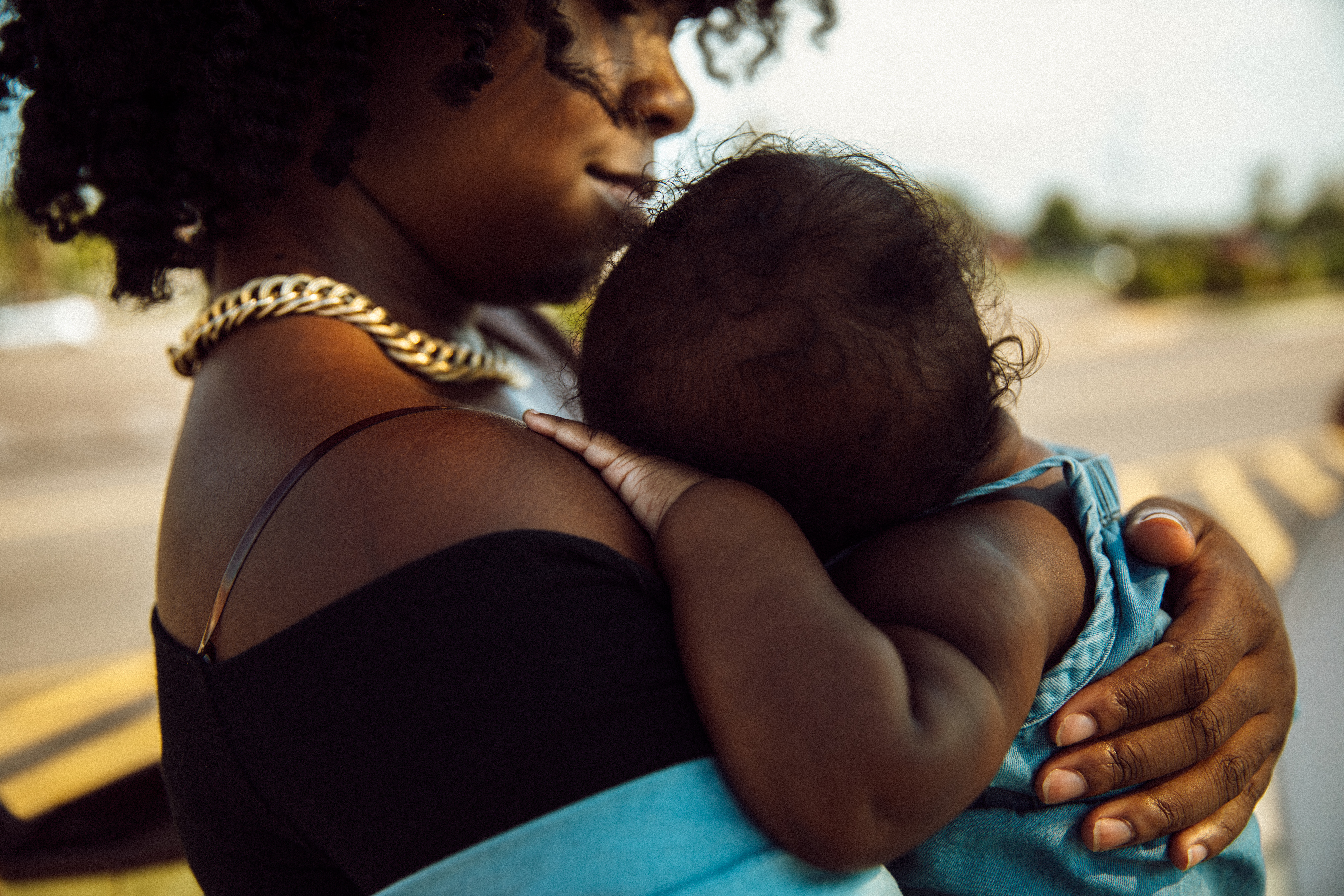 Janel Vee holds her infant daughter outside at a bus stop.