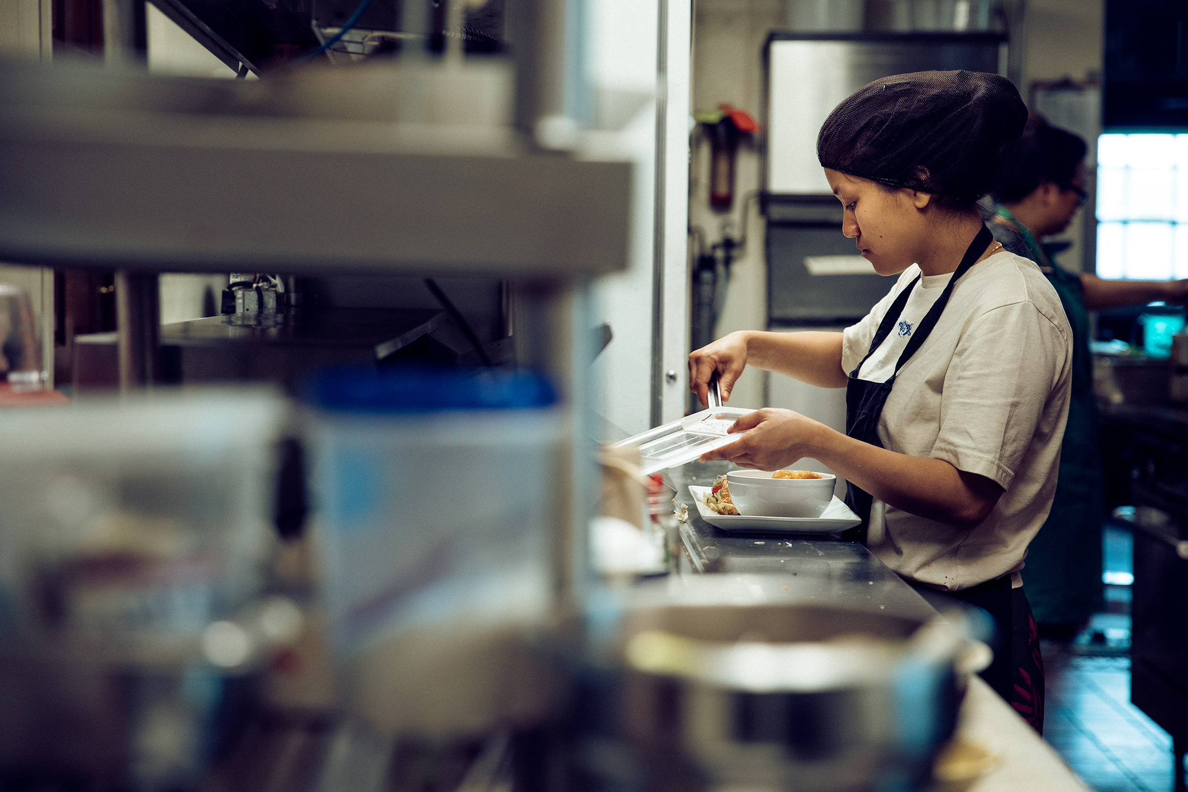 A female kitchen helper making a food dish at A plate of a noodle dish at Shwe Mandalay Burmese Cuisine in Battle Creek, Michigan.