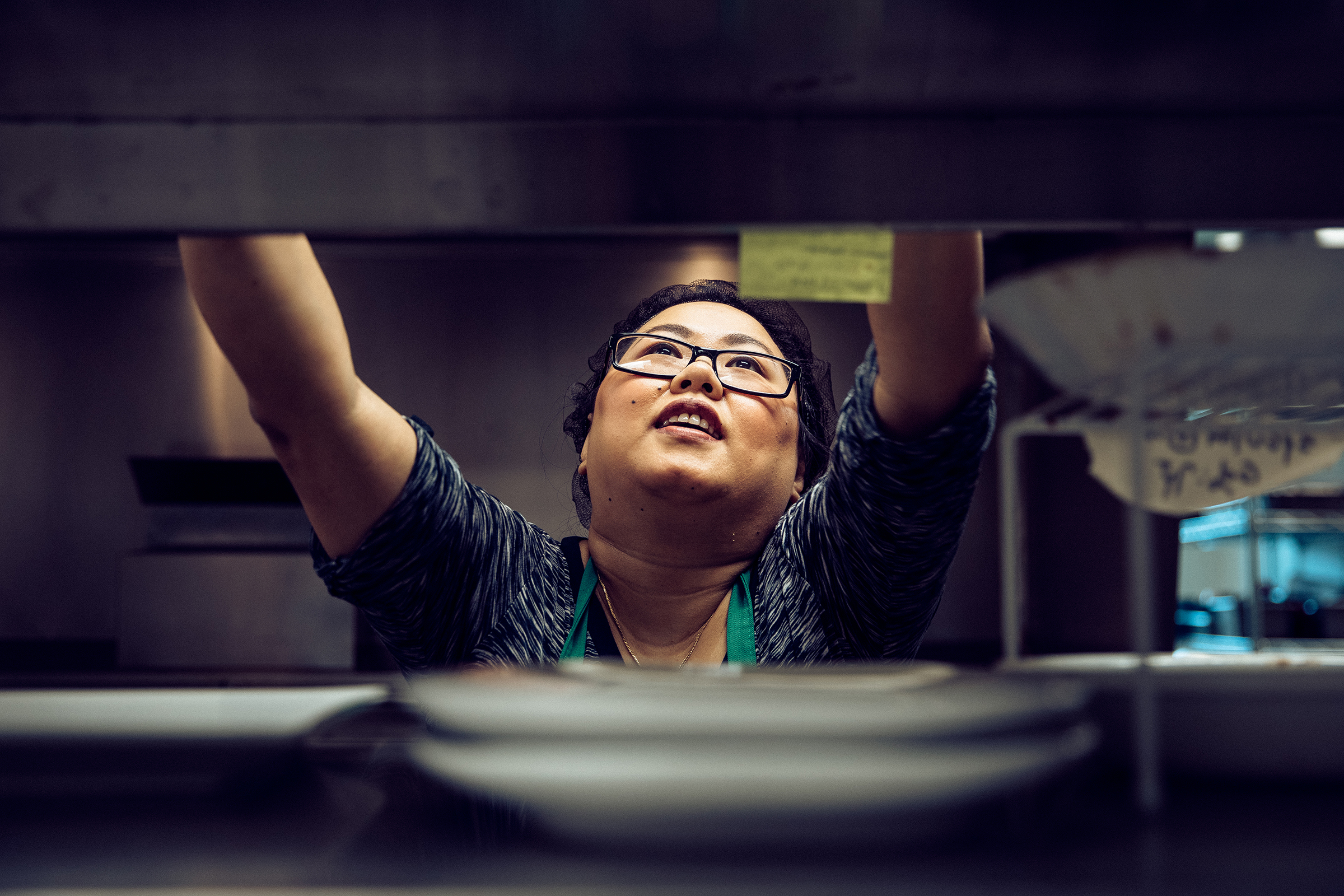 A woman reaching to grab an ingredient on the top shelf in the kitchen at the Shwe Mandalay Burmese Cuisine restaurant in Battle Creek, Michigan.