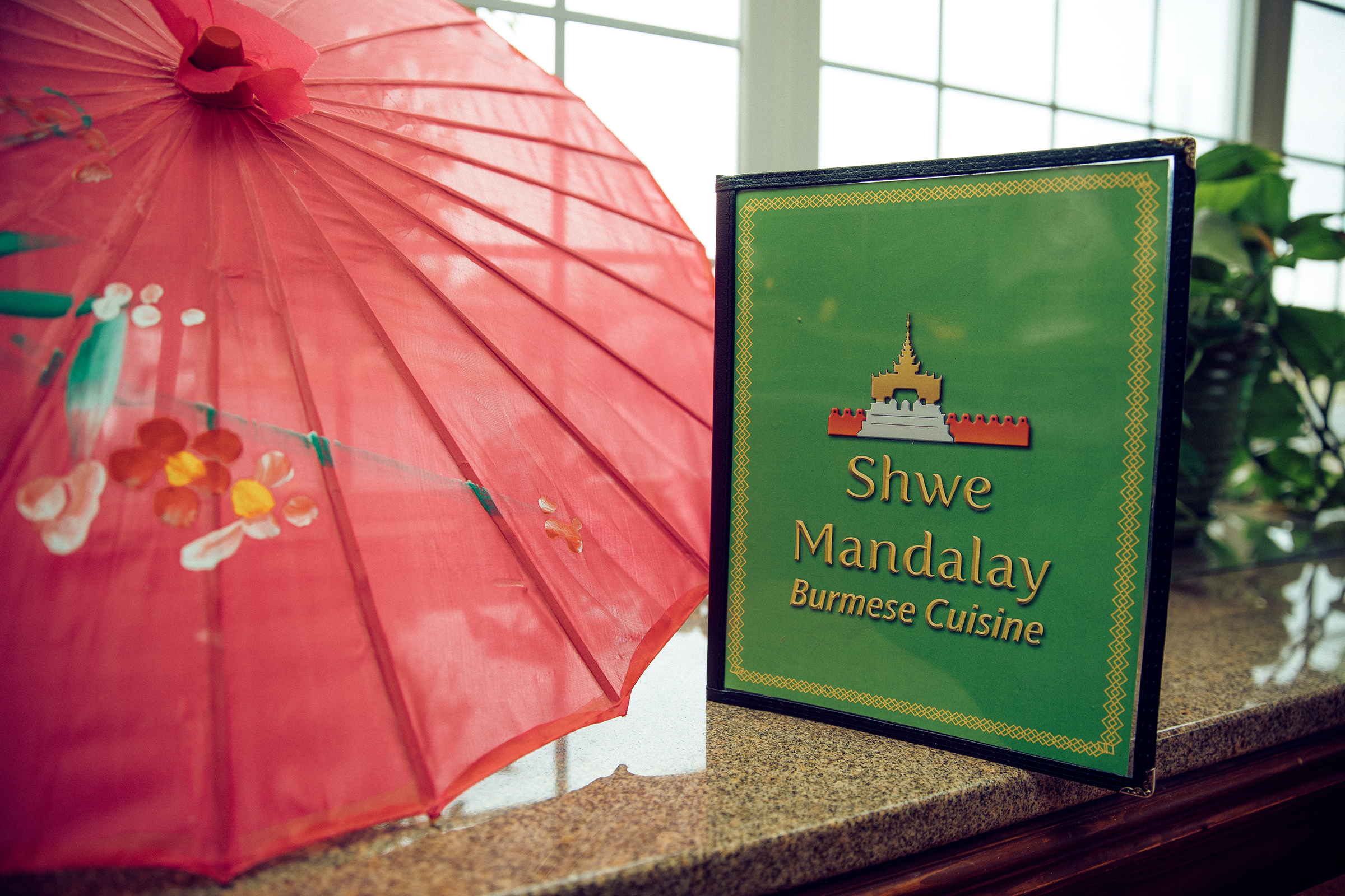 The Shwe Mandalay Burmese Cuisine restaurant menu next to a red traditional Asian umbrella in Battle Creek, Michigan.