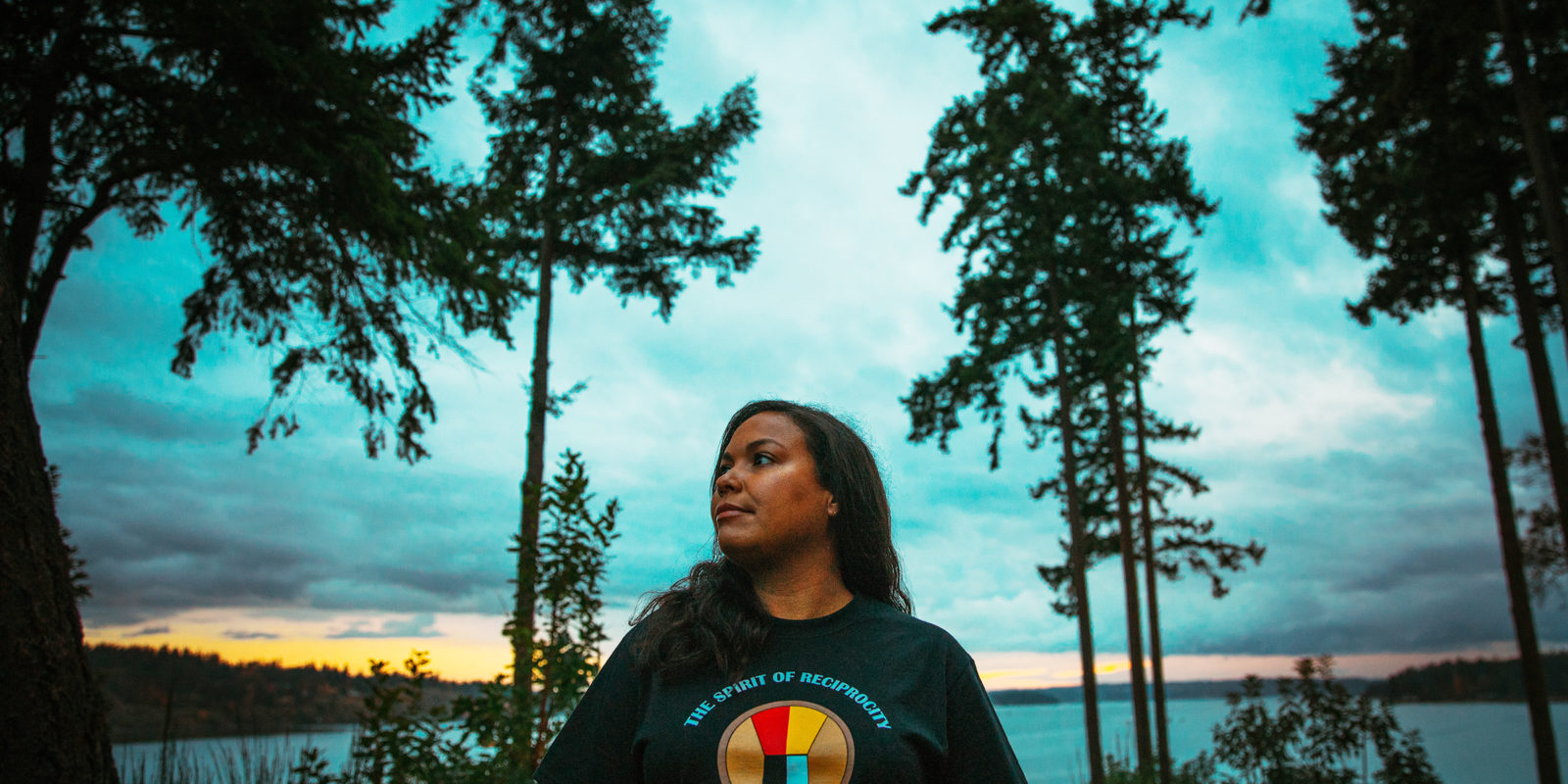 Potlatch Fund’s former Development and Communications Manager Damara Jacobs-Morris looking off to the left with the backdrop of trees and sea behind her. Potlatch Fund uplifts a longstanding native giving tradition to support community philantropy.