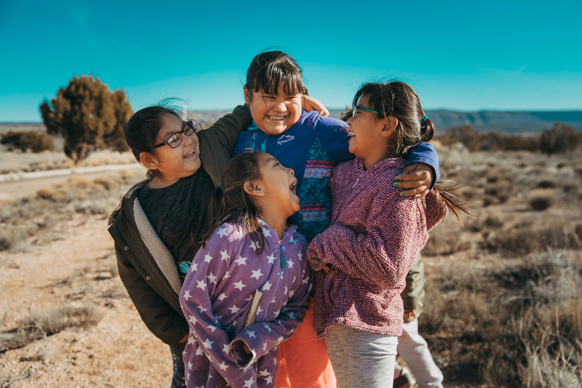 Four students looking at each other and laughing outside school at the Keres Children's Learning Center in New Mexico.