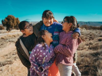 Four students looking at each other and laughing outside school at the Keres Children's Learning Center in New Mexico.
