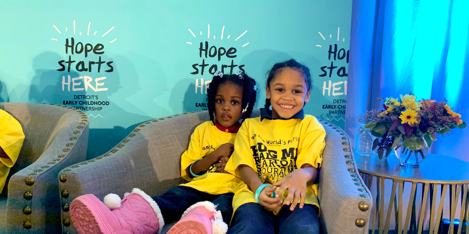 Two young children wearing yellow tshirts sitting on a chair at the Hope Starts Here Summit in Detroit.