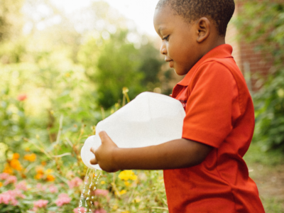 A young Black boy watering flowers outside in the school garden in New Orleans. Elisa Muñoz-Miller is ensuring that children and families in New Orleans have access to locally-sourced, healthy and affordable foods.