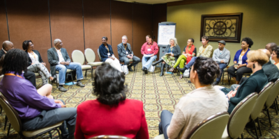 A group of diverse adults sitting in a circle and discussing racial equity.