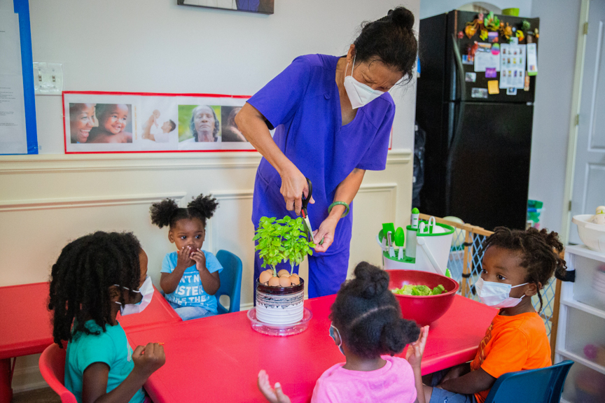An early care and education provider shows four children where fresh basil comes from while preparing salads for lunch at Lina Lane’s Learning Center in Ellenwood, GA. Photo courtesy of Quality Care for Children.