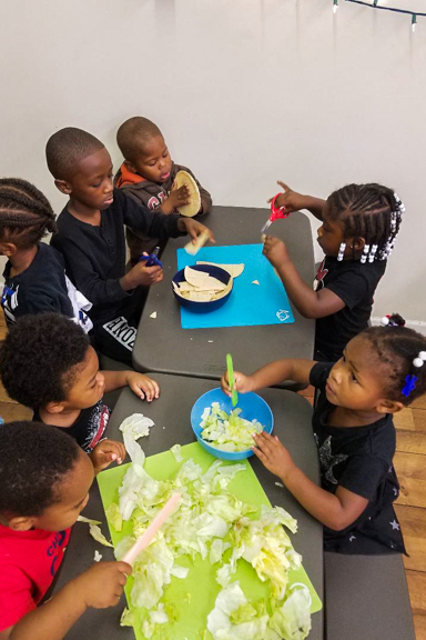 A group of kids help prepare lunch for the class by cutting lettuce and tortillas for tacos. Photo courtesy of WECA and Mother and Daughter Child Nurturing Center in Milwaukee, WI.