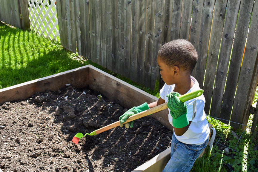 A young child wearing gardening gloves and using a small hoe to prepare the garden bed at A Mother’s Touch Center for Child Development in Sharon, PA. Photo courtesy of The Food Trust.