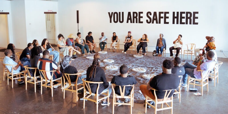 group of Black people sitting and talking in a circle with }You are safe here" on the wall | W.K. Kellogg Foundation