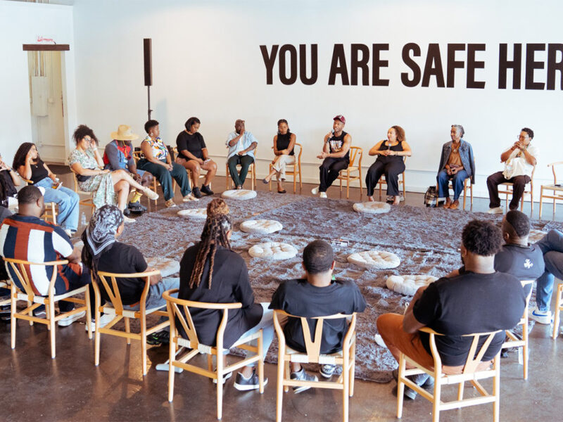 group of Black people sitting and talking in a circle with }You are safe here" on the wall | W.K. Kellogg Foundation