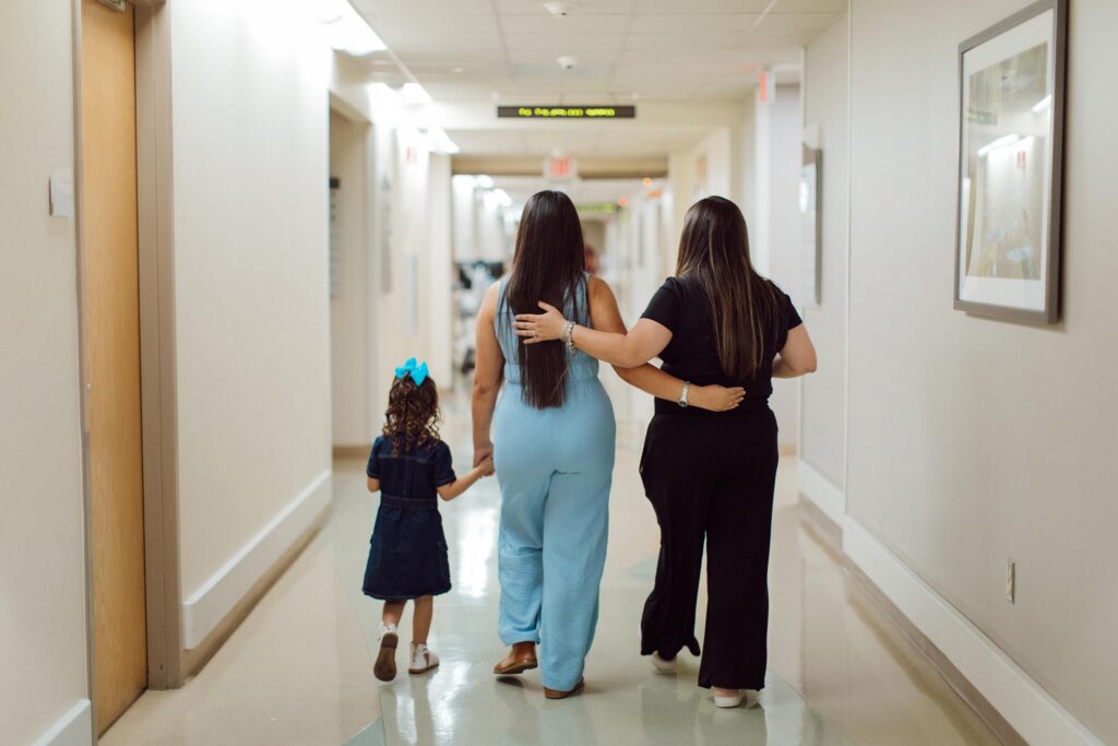 Two women walking down a hallway with a young child, arms around each other.