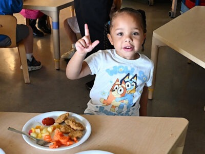 Child pointing up while sitting at table with a meal.